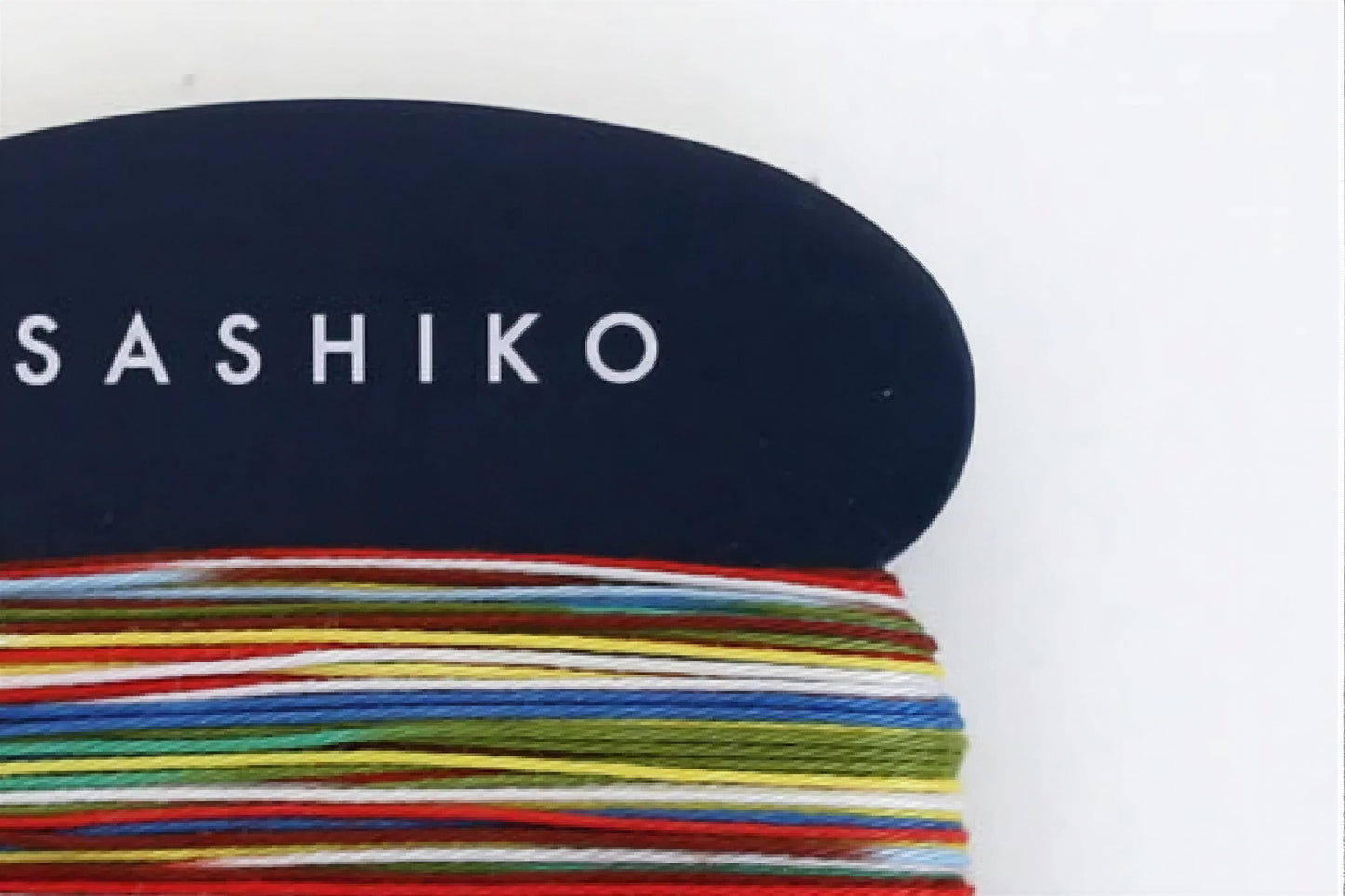 A close-up view of a black object with the word "SASHIKO" written on it, surrounded by a colorful array of yarn or thread in various shades and patterns.