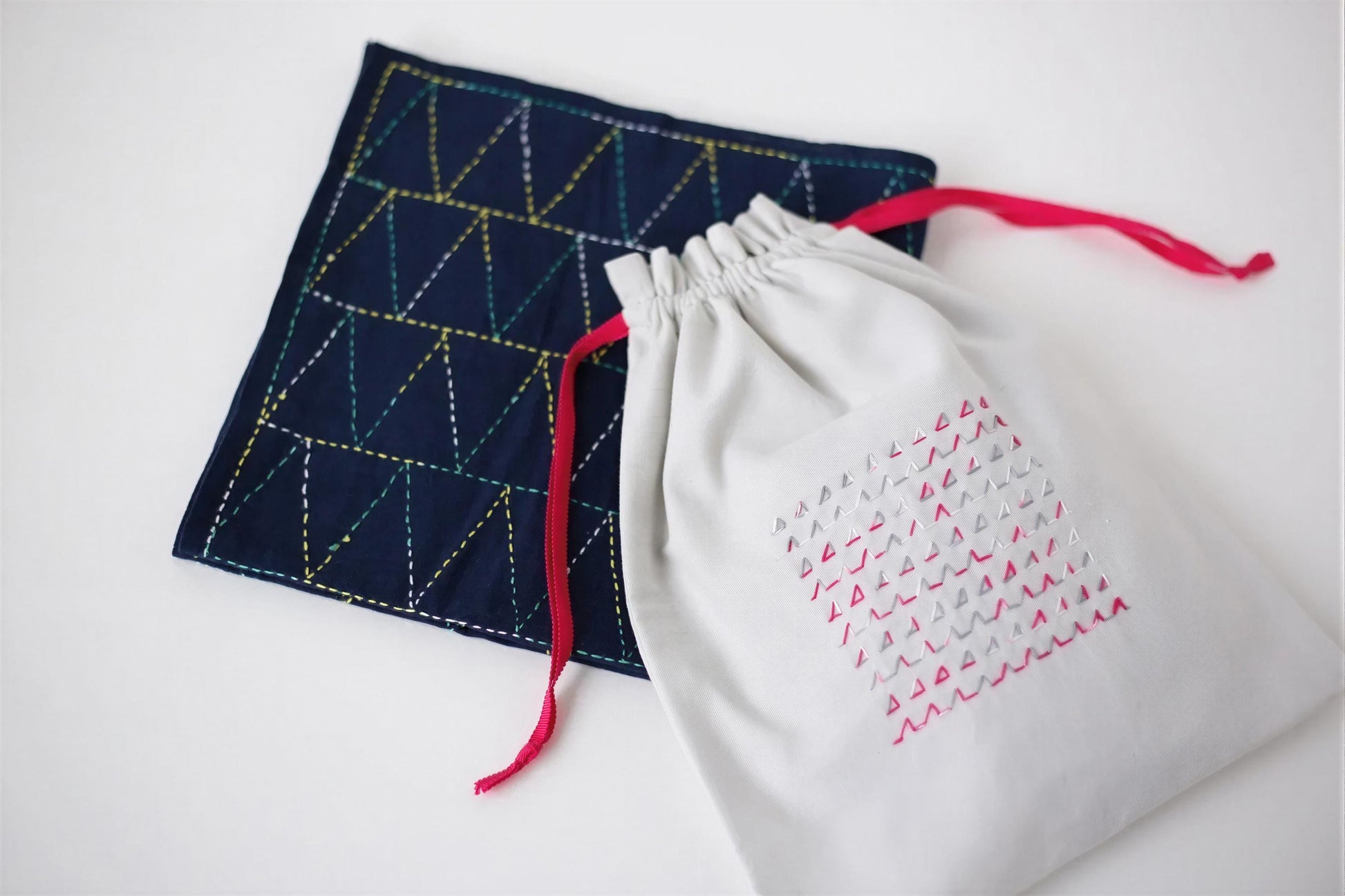 a white drawstring bag with a geometric pattern and a dark blue square with a red and yellow geometric pattern.
