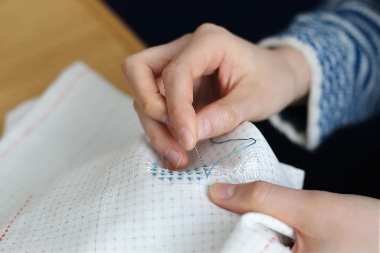 A person's hands are carefully stitching a pattern onto a piece of fabric using a needle and thread.
