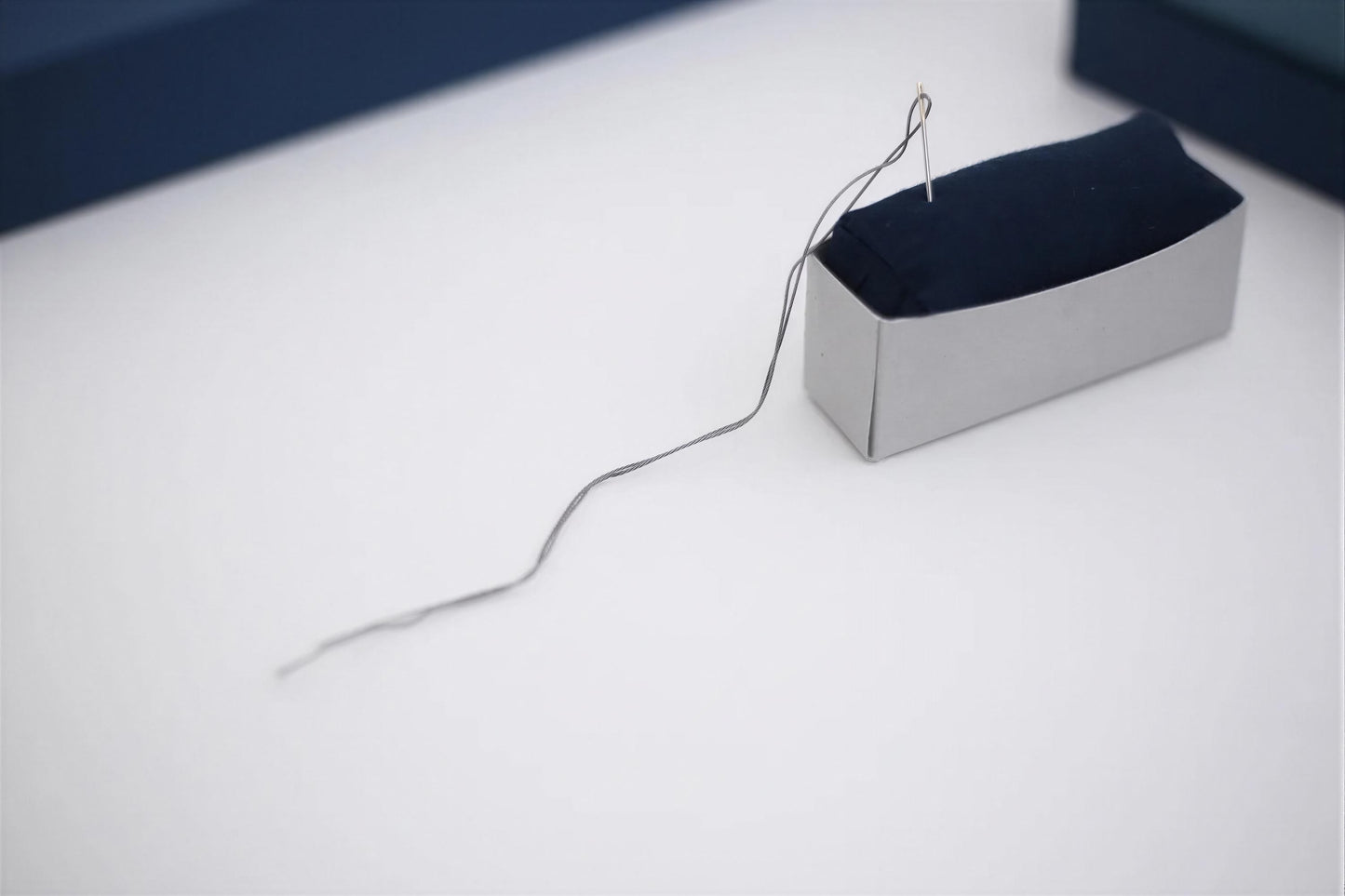 A small, rectangular box with a black fabric inside, and a single black thread or string extending from the box.