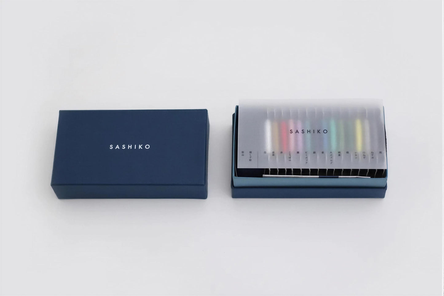 a blue box with the word "SASHIKO" written on it, and an open box containing a set of colored pencils with the word "SASHIKO" printed on them.