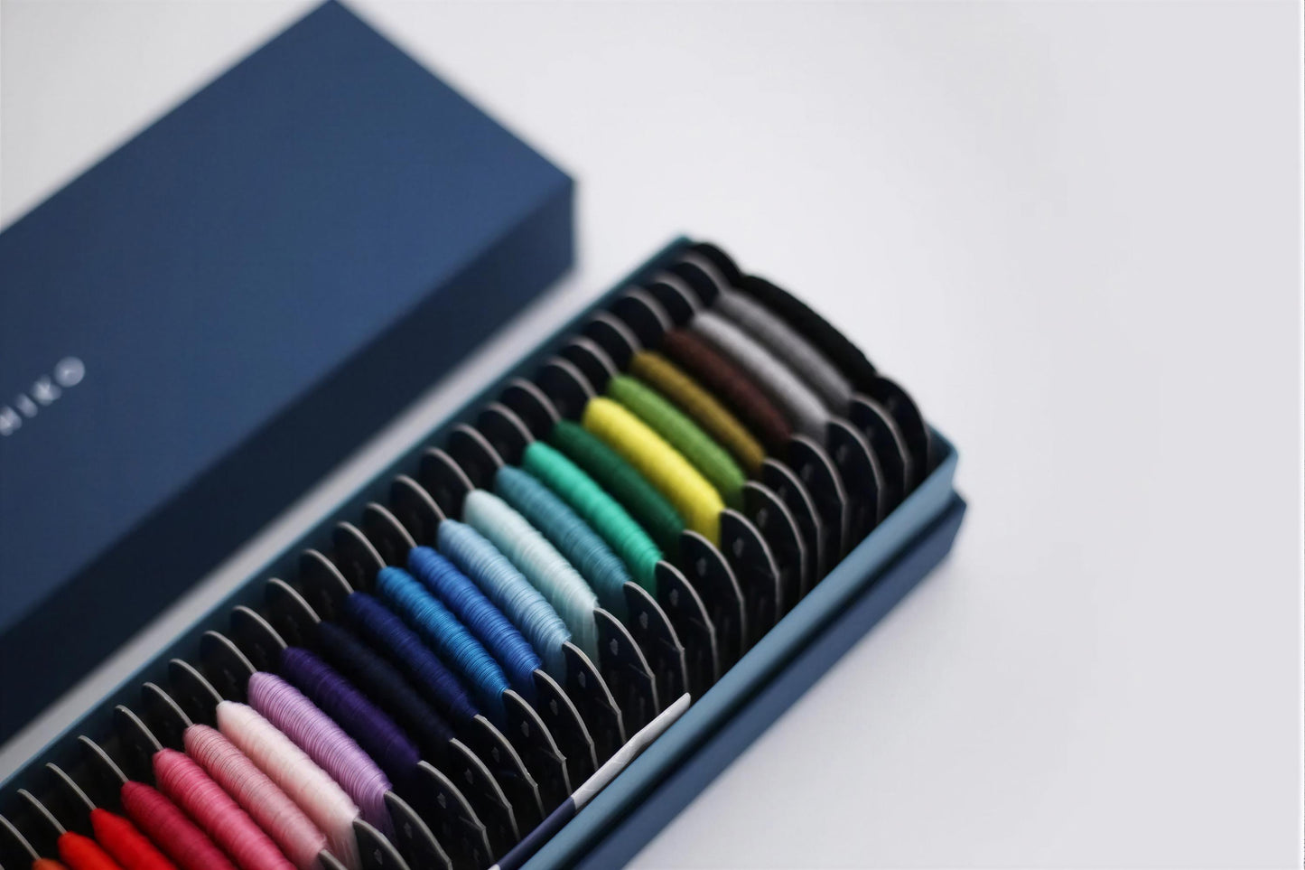 A blue box containing a variety of colorful spools of thread or yarn, arranged in rows.