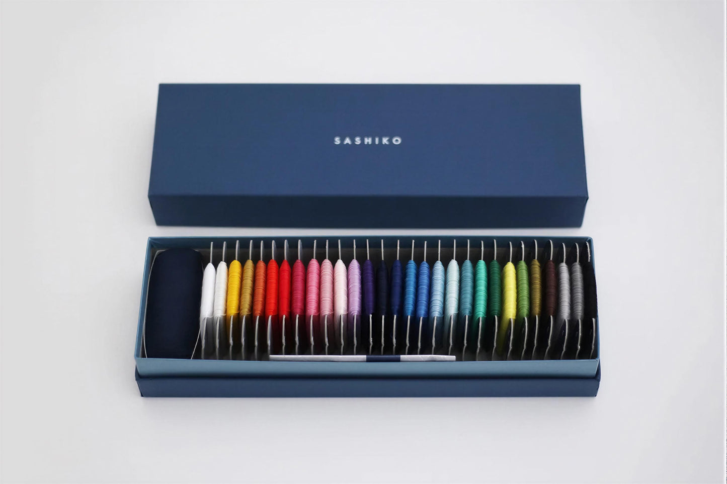 A blue box containing a collection of colorful spools of thread, with the brand name "SASHIKO" printed on the box lid.