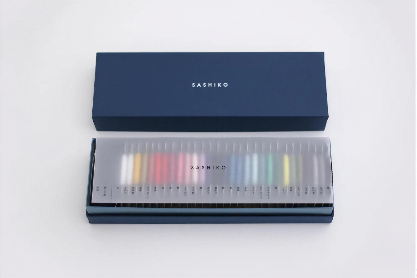 A blue box with the word "SASHIKO" printed on it, and a transparent display case containing a row of colorful pencils.