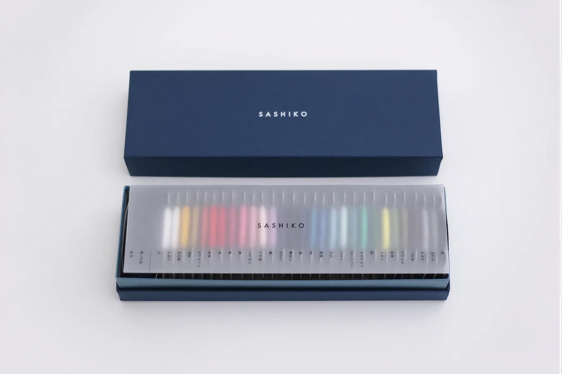 A blue box with the word "SASHIKO" printed on it, and a transparent display case containing a row of colorful pencils.