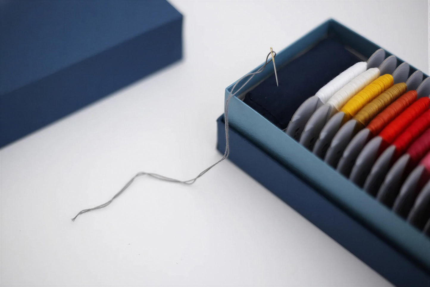 A blue box containing a variety of colorful spools of thread, with a single spool of thread visible sticking out of the box.