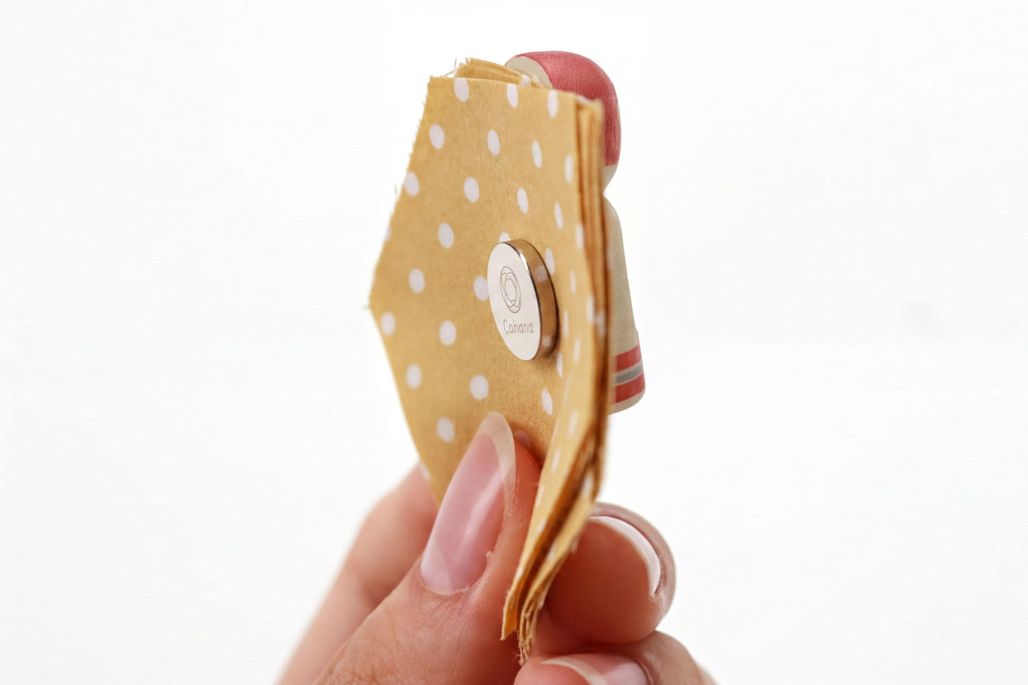 A hand holding a yellow fabric with white polka dots, with a small metal object attached to it.
