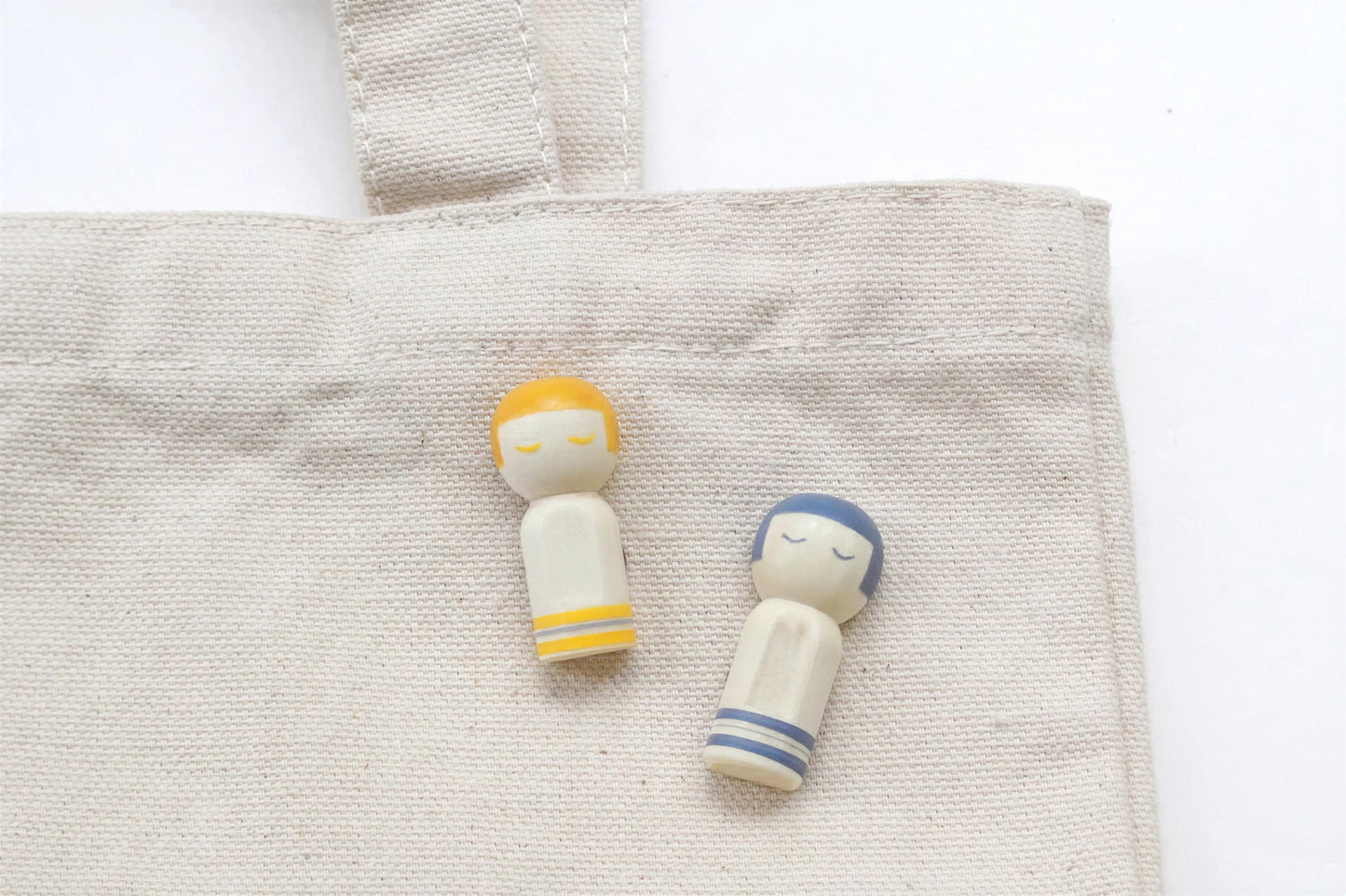 Two small wooden figurines, one yellow and one blue, are placed on a beige fabric surface.