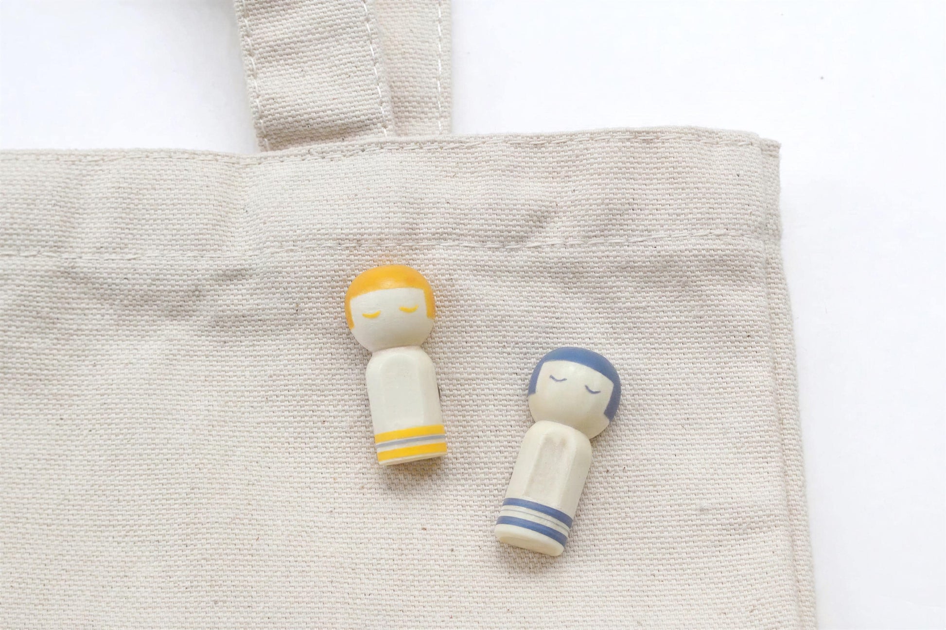 Two small wooden figurines, one yellow and one blue, are placed on a beige fabric surface.