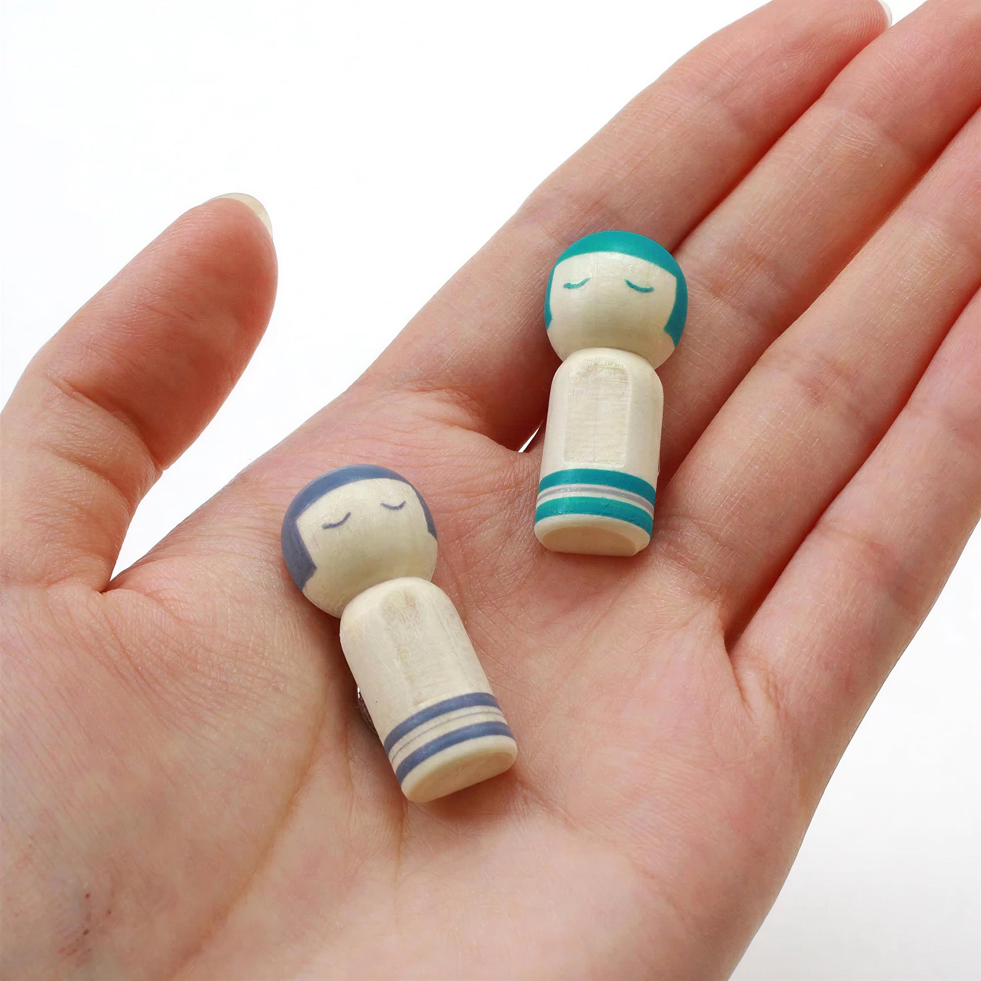 A hand holding two small wooden dolls with blue and white striped ribbons.