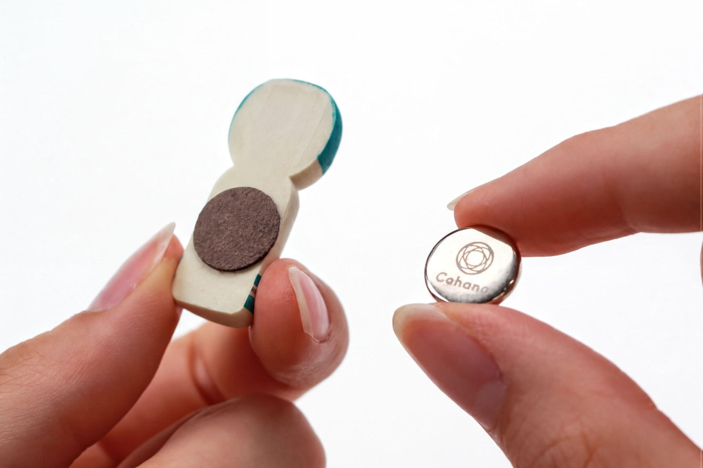 A person's fingers are holding a small wooden object with a magnet on it, and a small metal object with a logo on it.