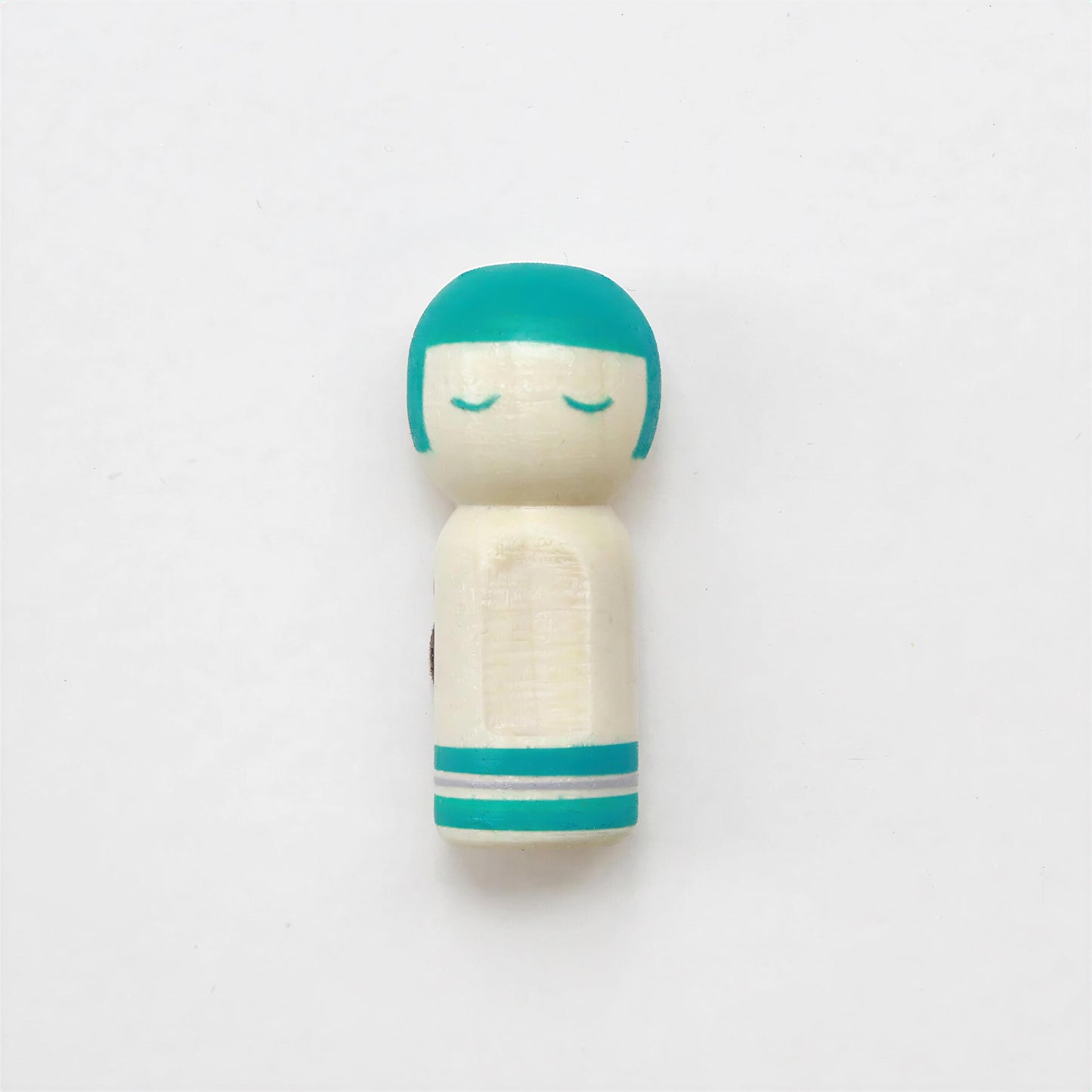 A small wooden doll with a turquoise head and white body, standing alone against a plain white background.