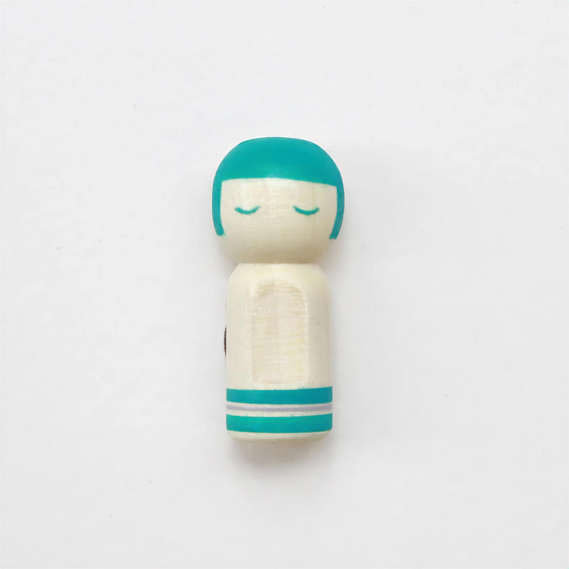 A small wooden doll with a turquoise head and white body, standing alone against a plain white background.