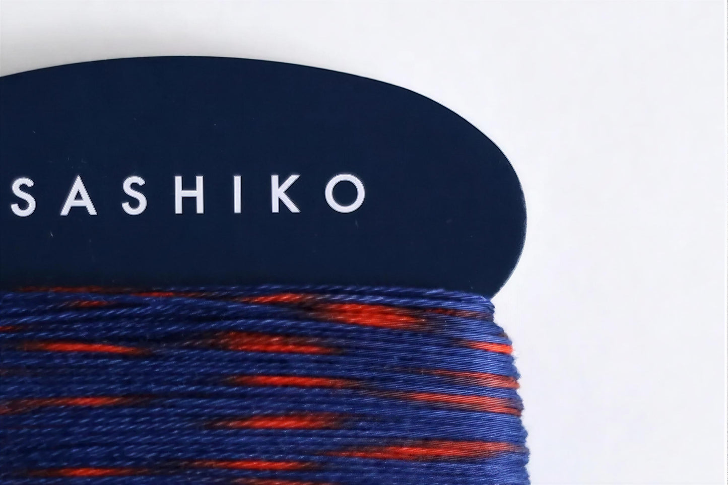 A close-up view of a blue and orange yarn skein, with the word "SASHIKO" printed on a dark blue background.