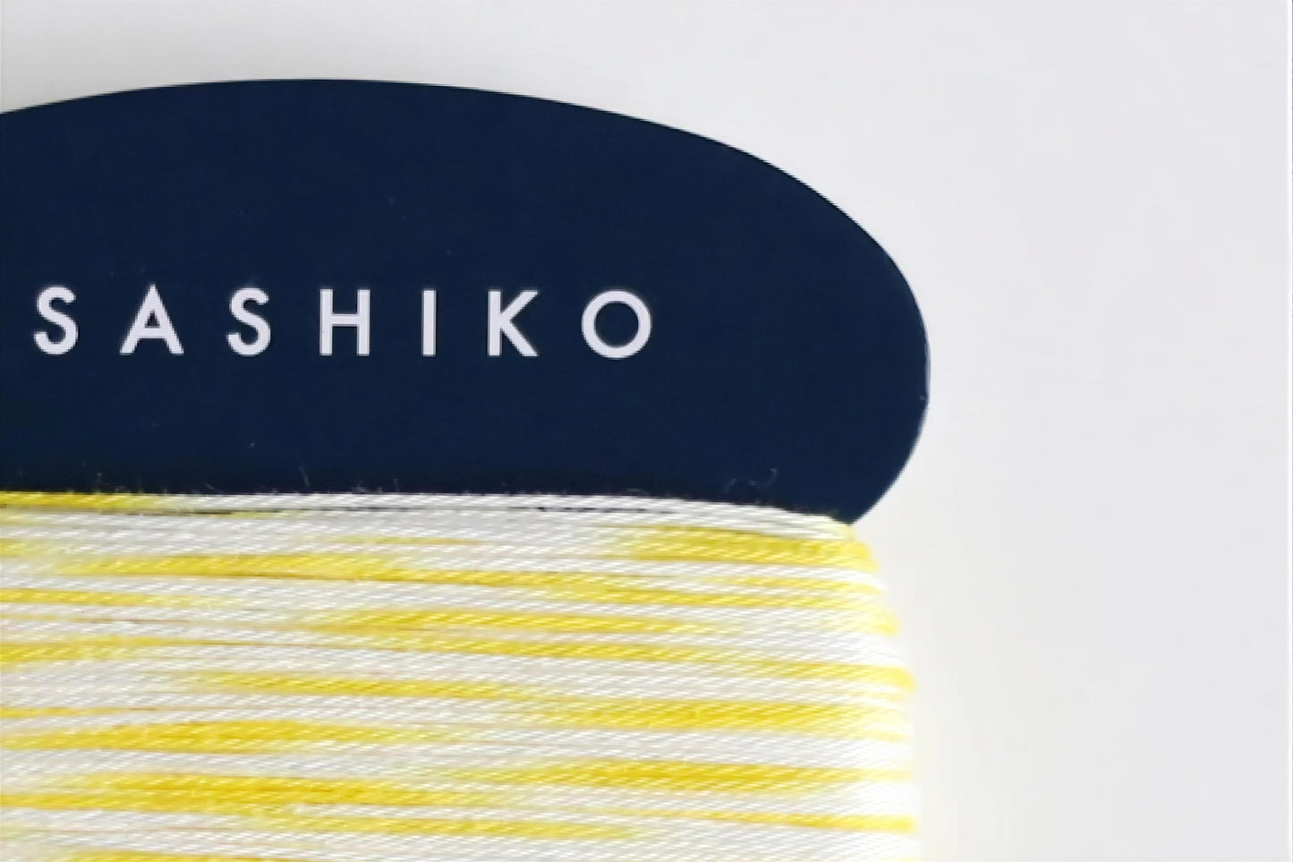 A close-up view of a blue object with the word "SASHIKO" written on it, along with a spool of yellow and white yarn.