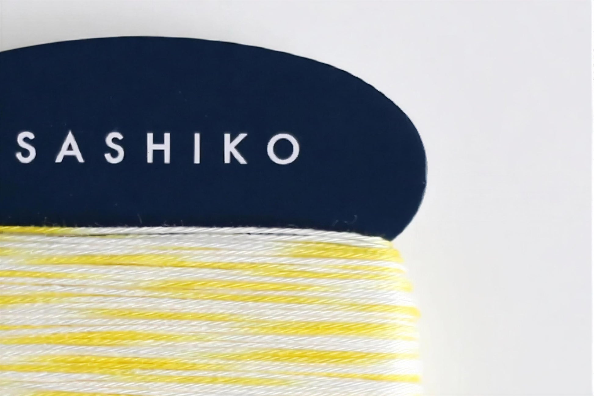 A close-up view of a blue object with the word "SASHIKO" written on it, along with a spool of yellow and white yarn.