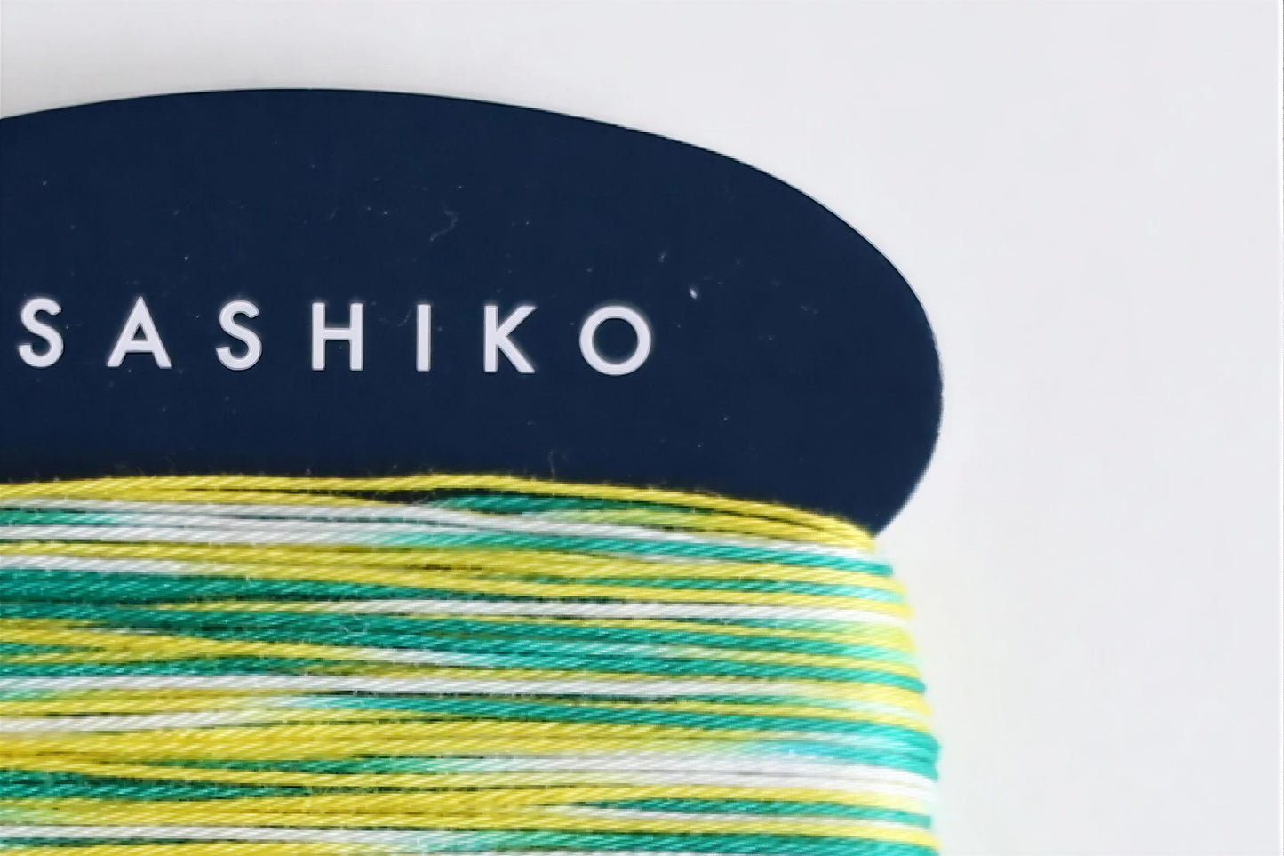 A close-up view of a spool of multicolored yarn with the brand name "SASHIKO" printed on a dark blue background.