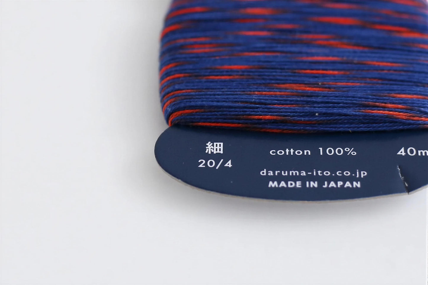 a close-up view of a spool of thread with a label indicating the cotton content and the brand.