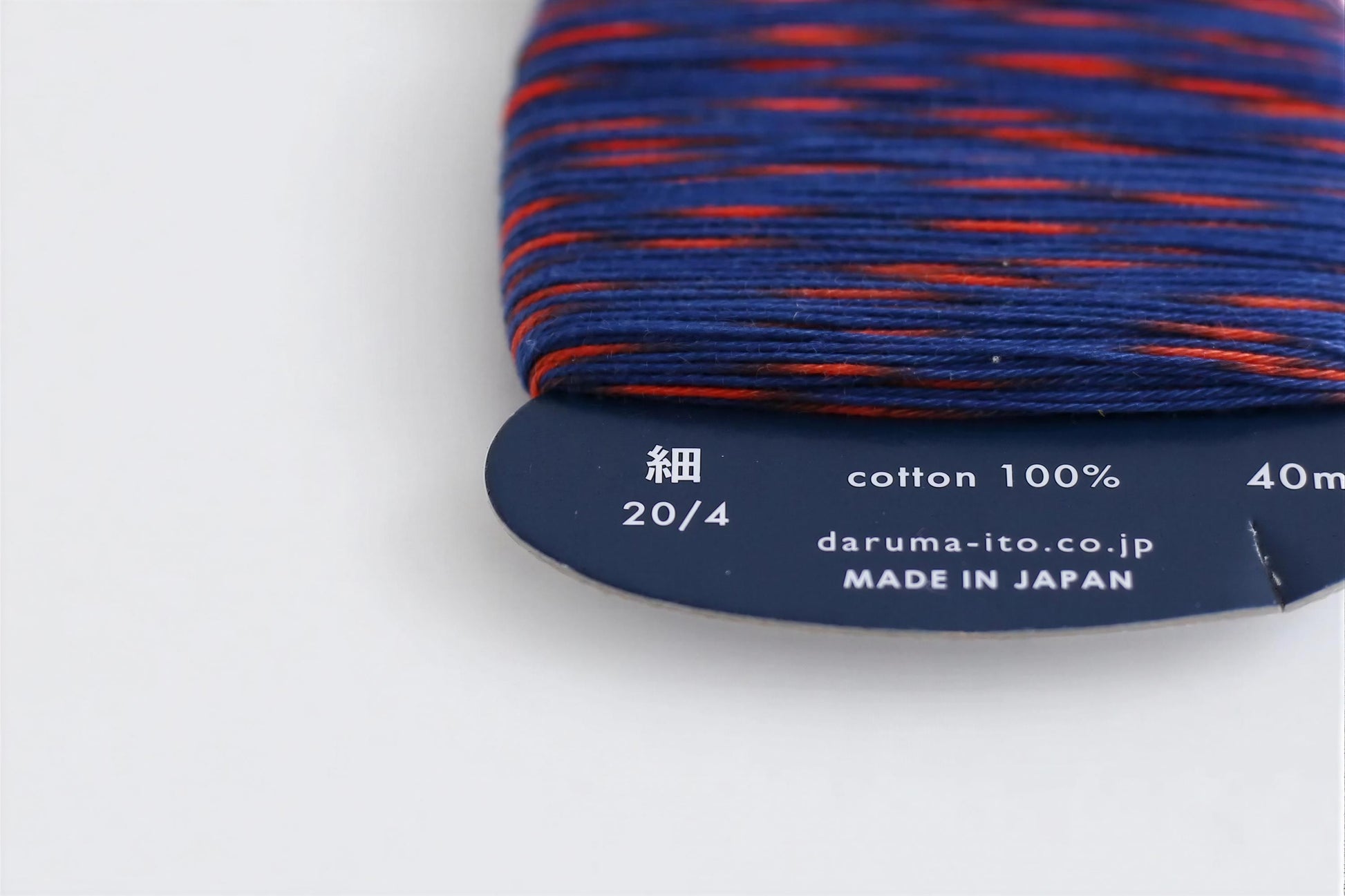 a close-up view of a spool of thread with a label indicating the cotton content and the brand.