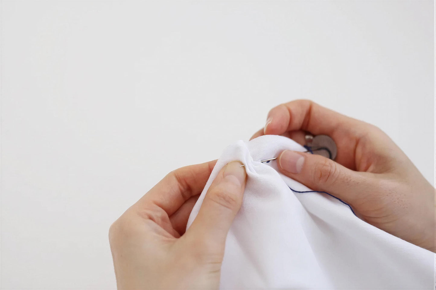 A pair of hands carefully sewing a white fabric with a needle and thread.