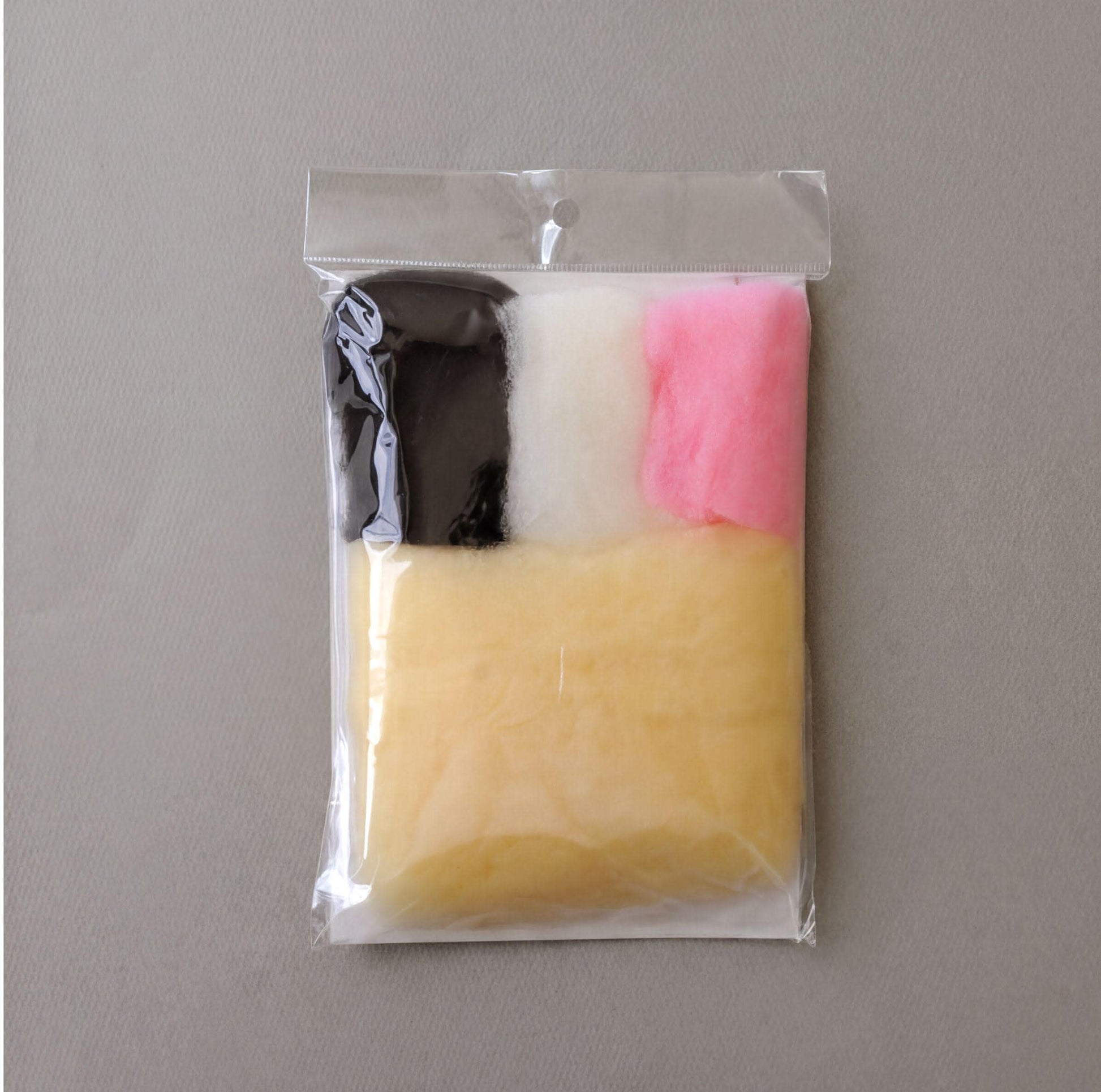 A clear plastic bag containing a variety of colorful cotton balls, including black, pink, and yellow, arranged in a square pattern.