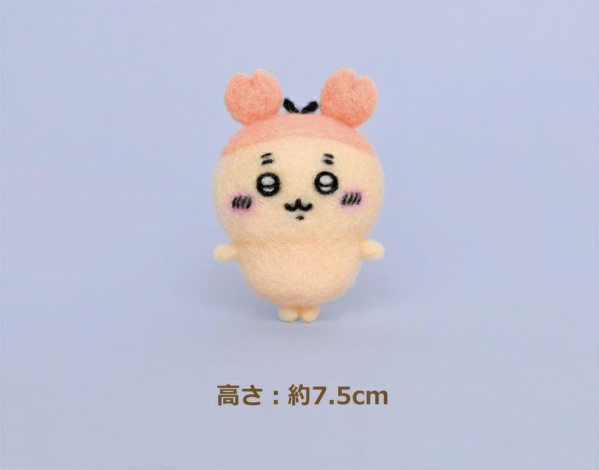 A small, cute plush toy with a pink hat and face, standing on a plain background.