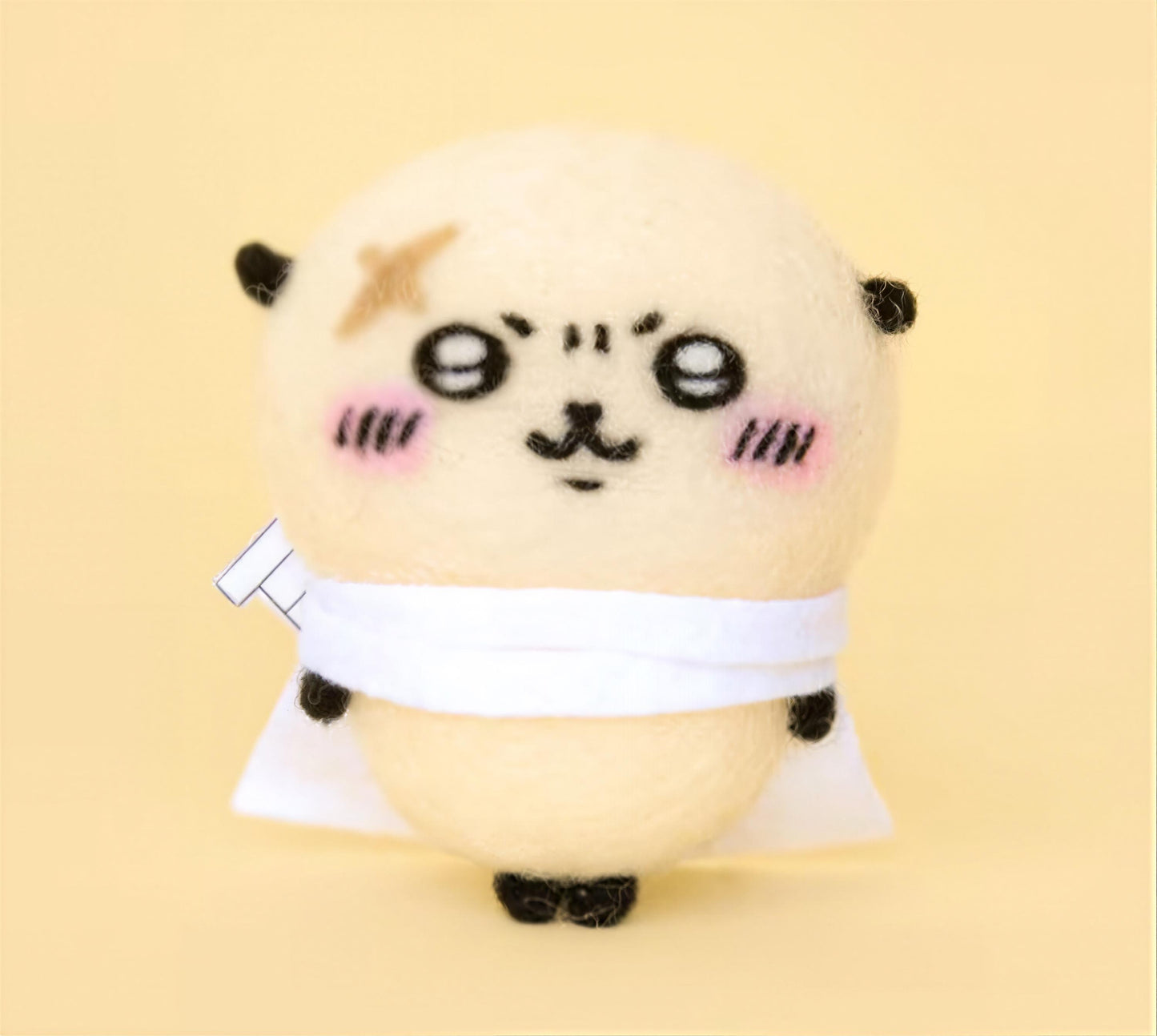A cute, hand-made plush toy with a round body, large eyes, and a small nose, wearing a white scarf and standing on a yellow background.