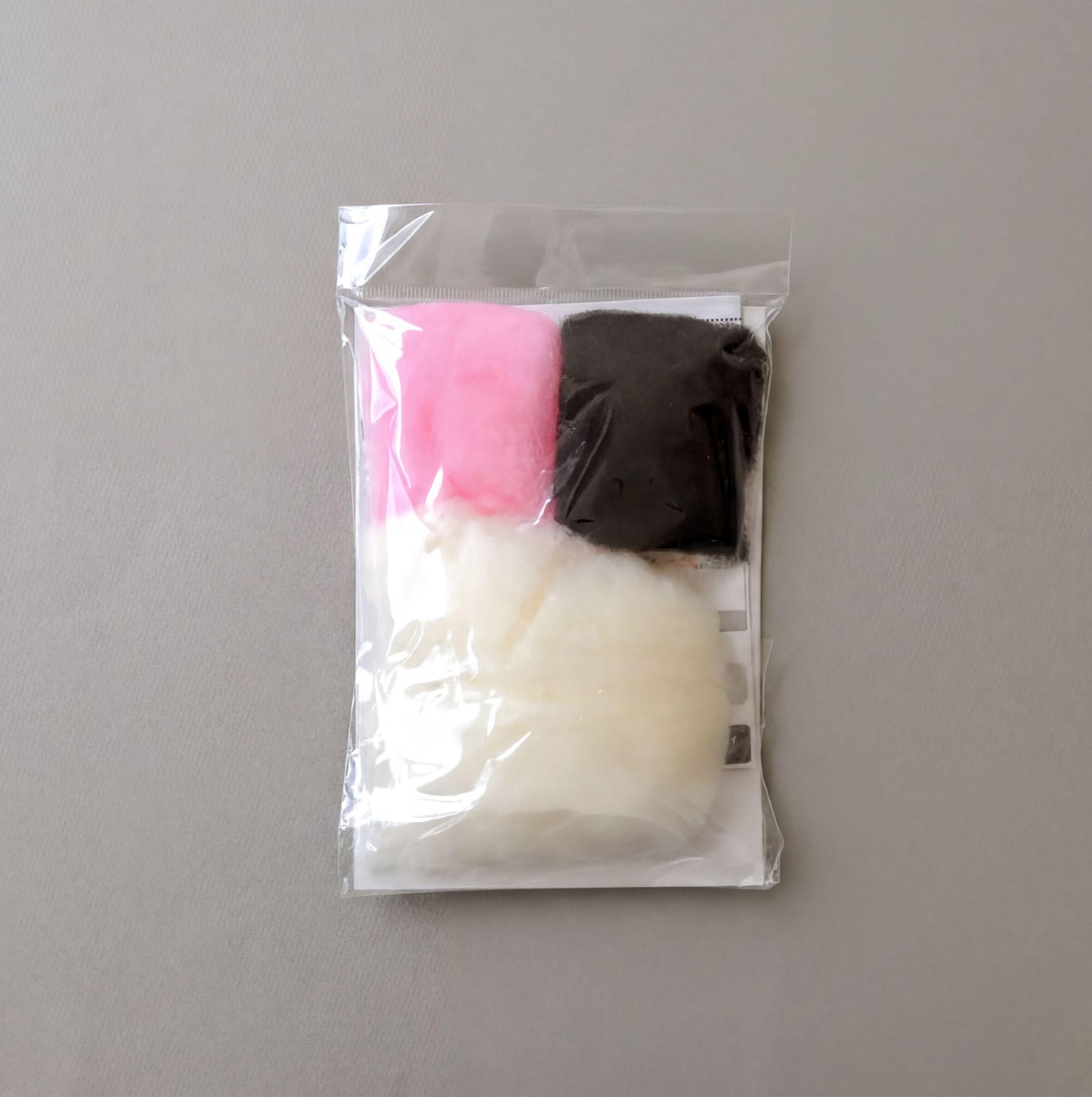 A clear plastic bag containing three different colored balls, including a pink one, a black one, and a white one.