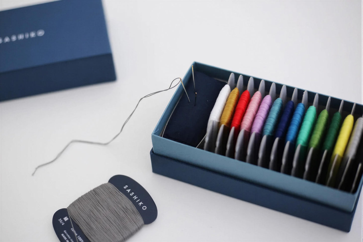 a blue box containing a variety of colorful thread spools, with a spool of gray thread and a spool of black thread visible on the left side.