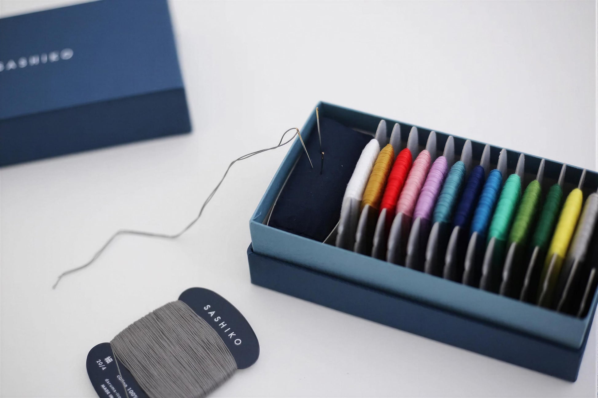 a blue box containing a variety of colorful thread spools, with a spool of gray thread and a spool of black thread visible on the left side.