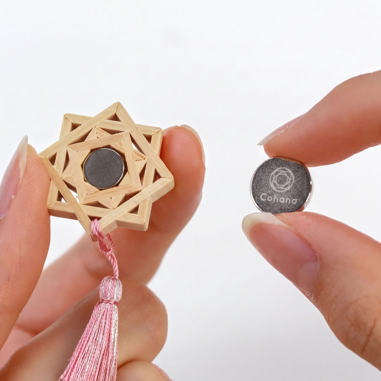 A person's hand holding a wooden star-shaped object with a tassel attached, and a small metal object with a logo on it.