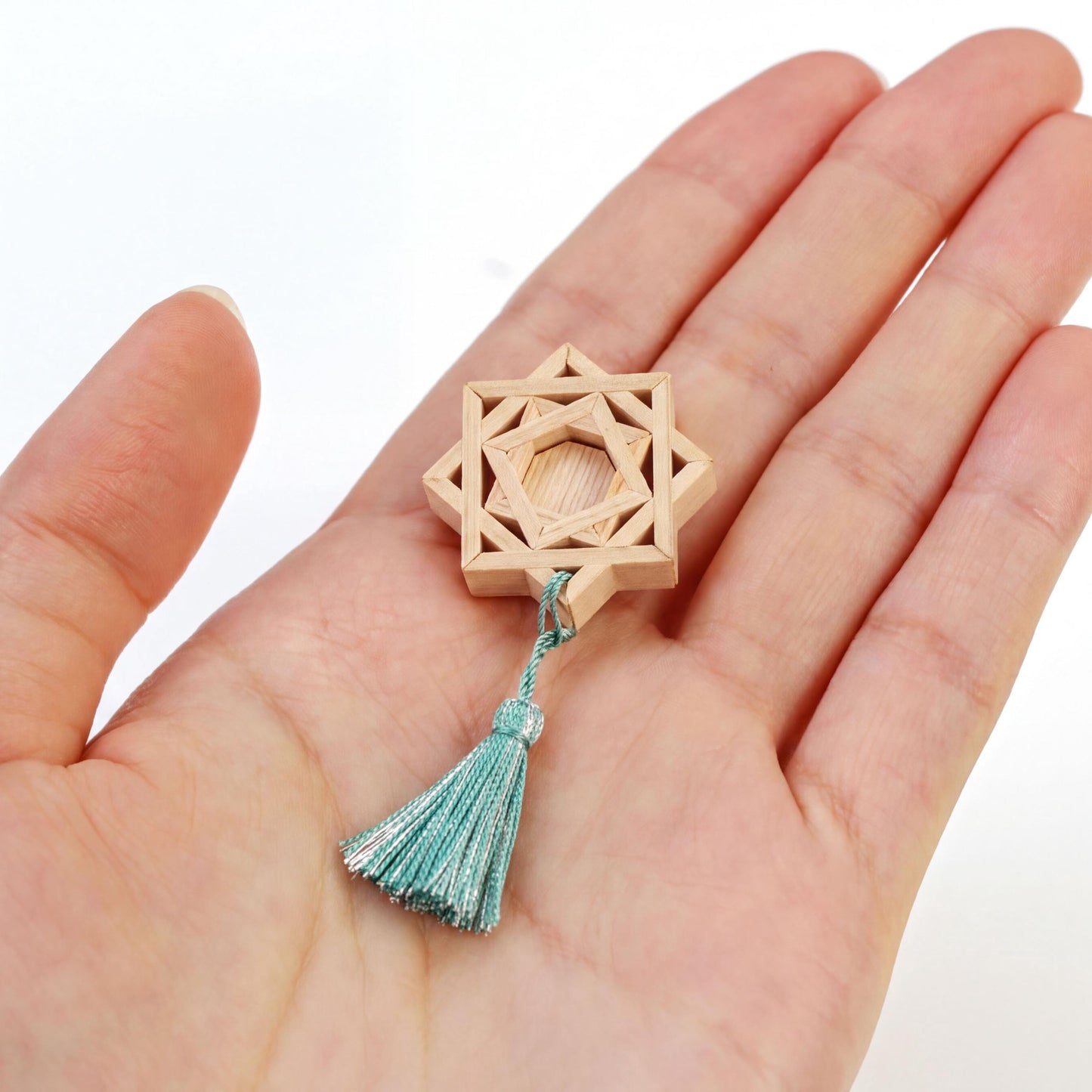 A hand holding a wooden star-shaped object with a tassel attached to it.