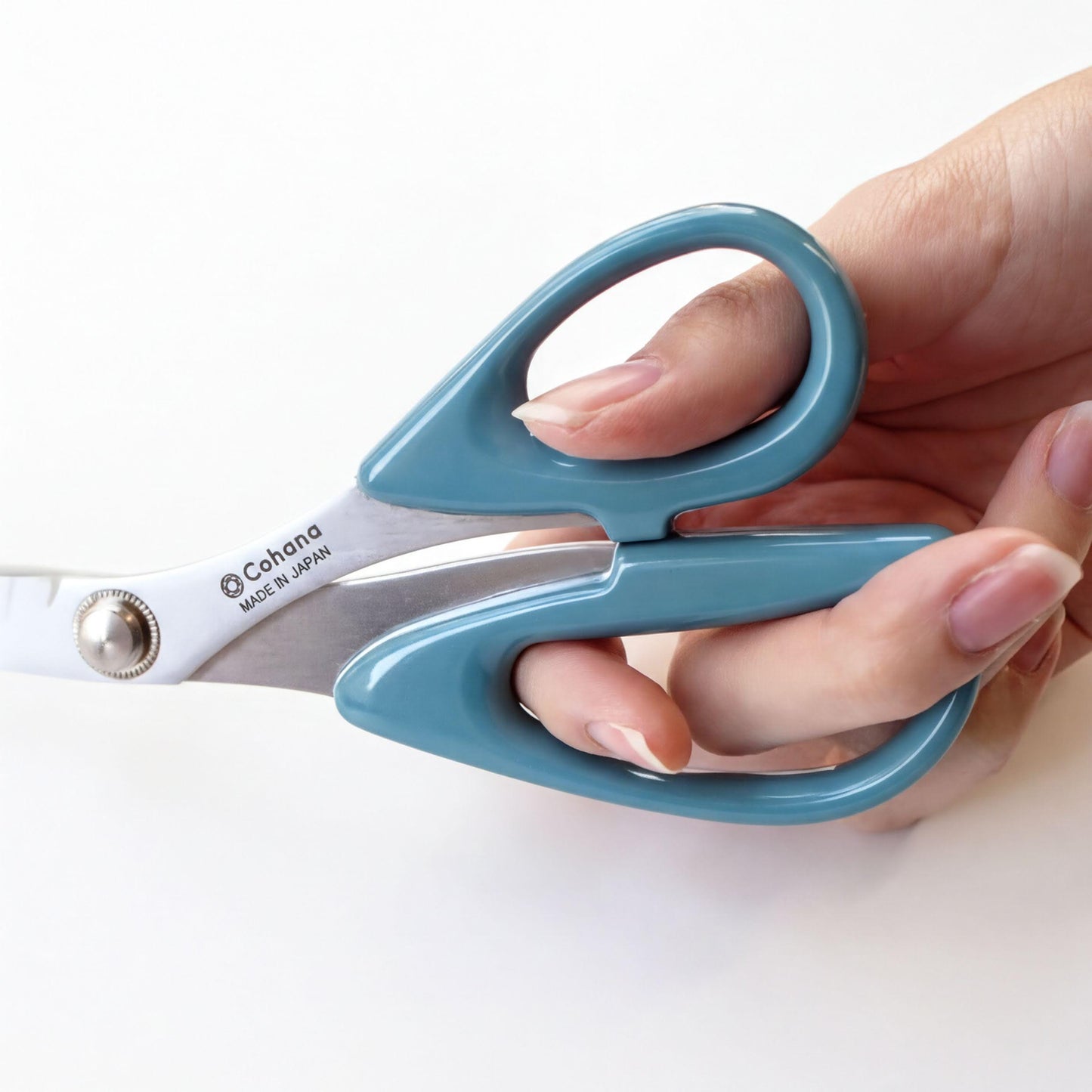 A hand holding a pair of blue-handled scissors with the brand name "Colona" printed on the blades.