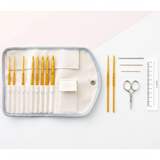 A crochet set consisting of a white case with a zipper, a ruler, a pair of scissors, and a pair of crochet hooks is arranged on a white background.