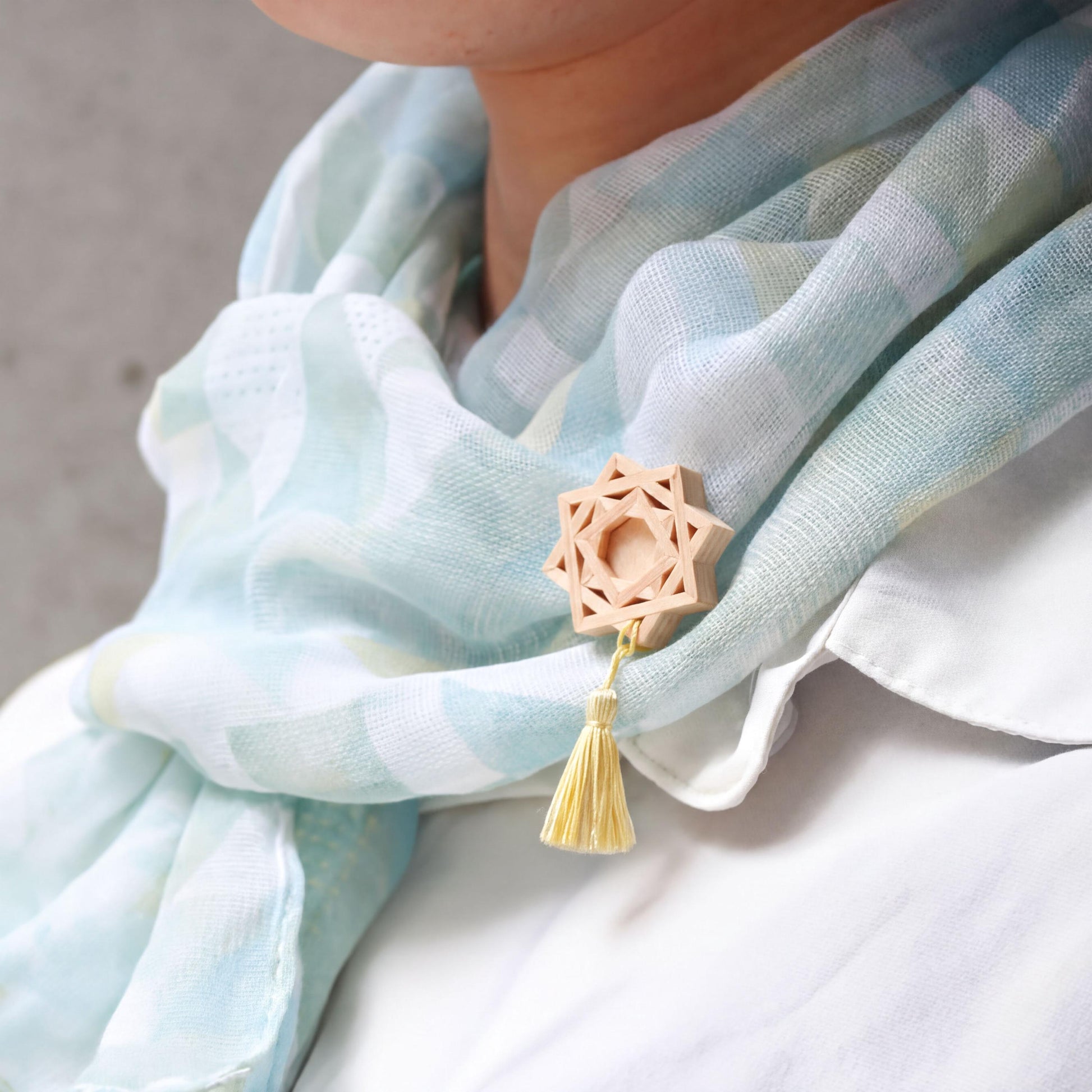 A person wearing a light blue scarf with a wooden star-shaped pendant and a yellow tassel.