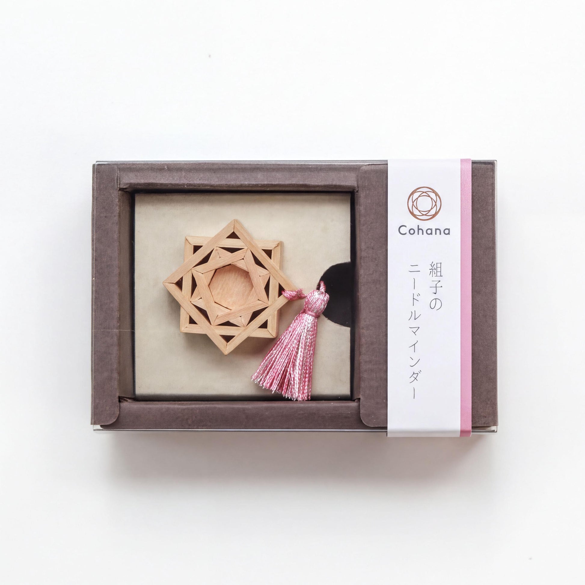 A wooden star-shaped ornament with a pink tassel, displayed in a brown box with a label that includes Japanese text.