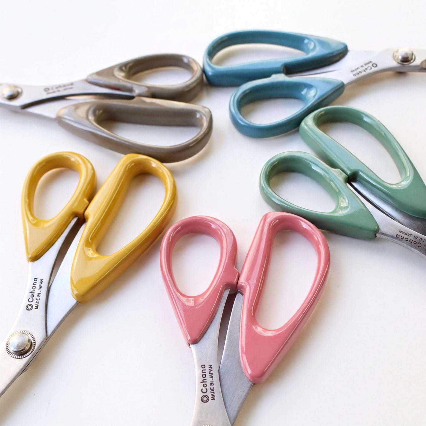 A collection of colorful scissors with various designs and colors, including yellow, pink, blue, and green, arranged on a white background.