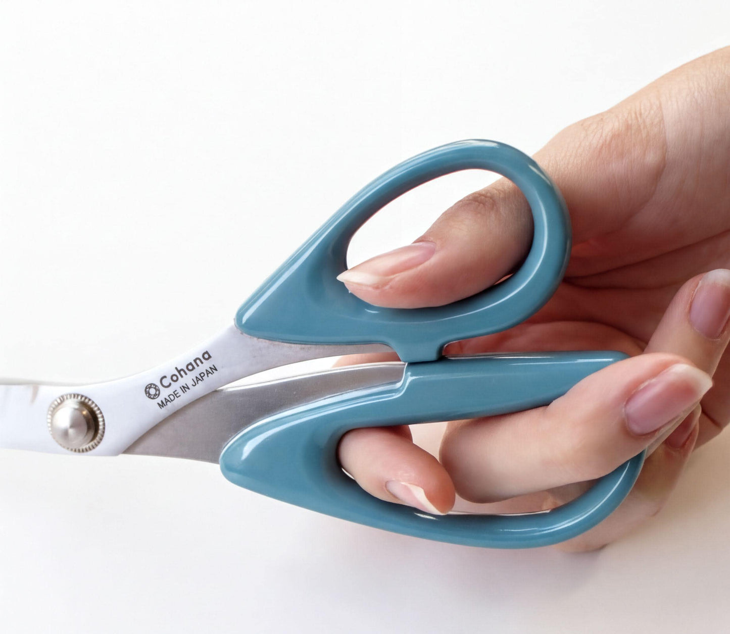 A hand holding a pair of blue-handled scissors with the brand name "Cohana" visible on the blades.