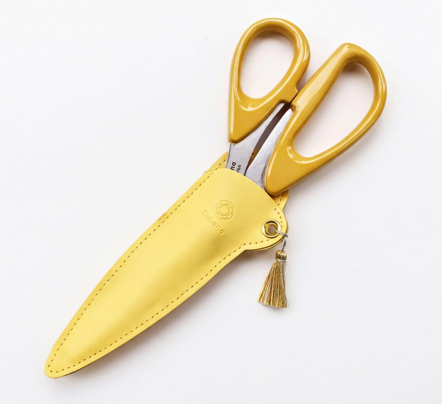 A pair of yellow scissors with a tassel hanging from the handle, placed in a yellow leather case.