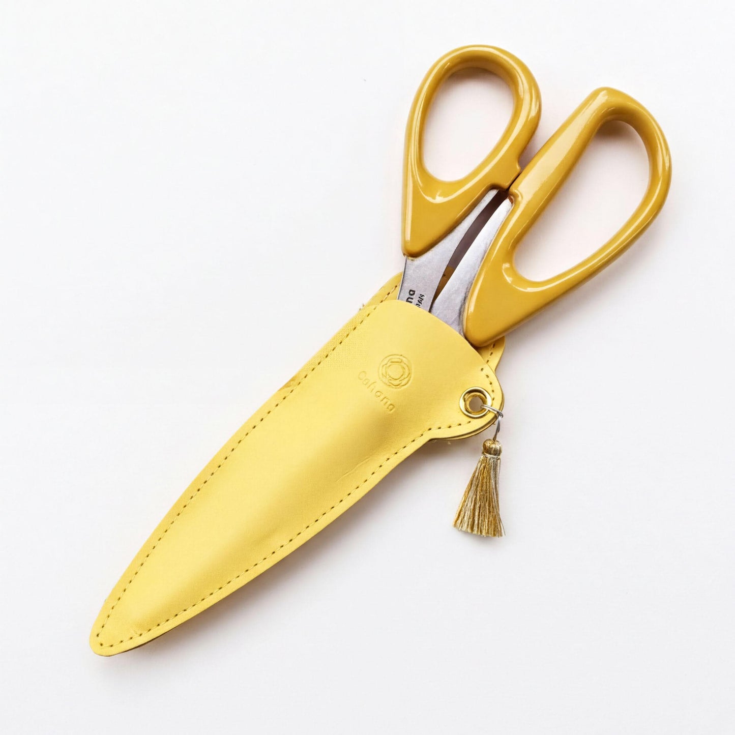 A pair of yellow scissors with a tassel hanging from the handle, placed in a yellow leather case.