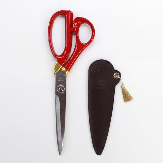A pair of red scissors with gold accents and a black leather case are shown against a white background.