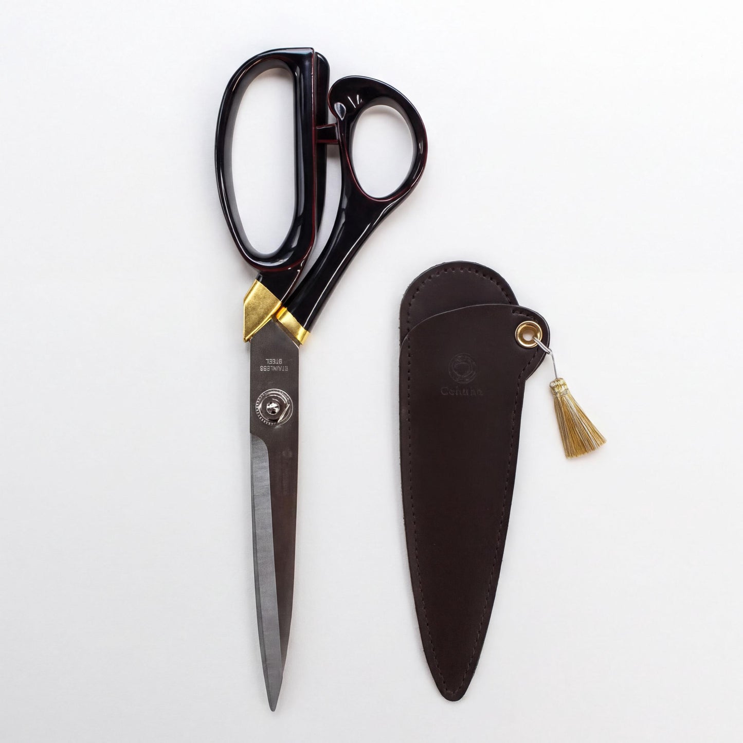 A pair of black and gold scissors with a leather case and tassel is shown against a white background.