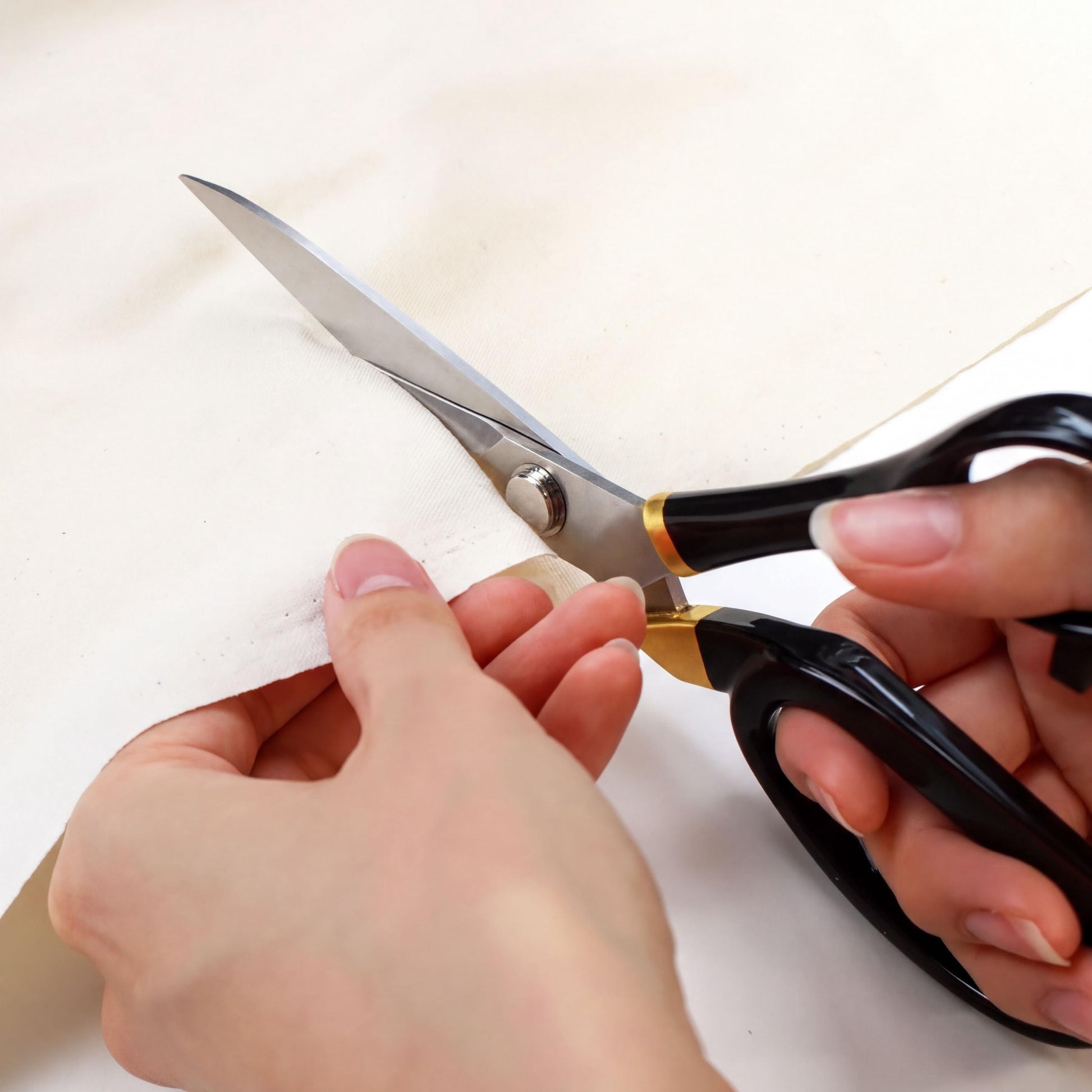 A person's hands are holding a pair of black scissors and cutting a piece of white fabric.