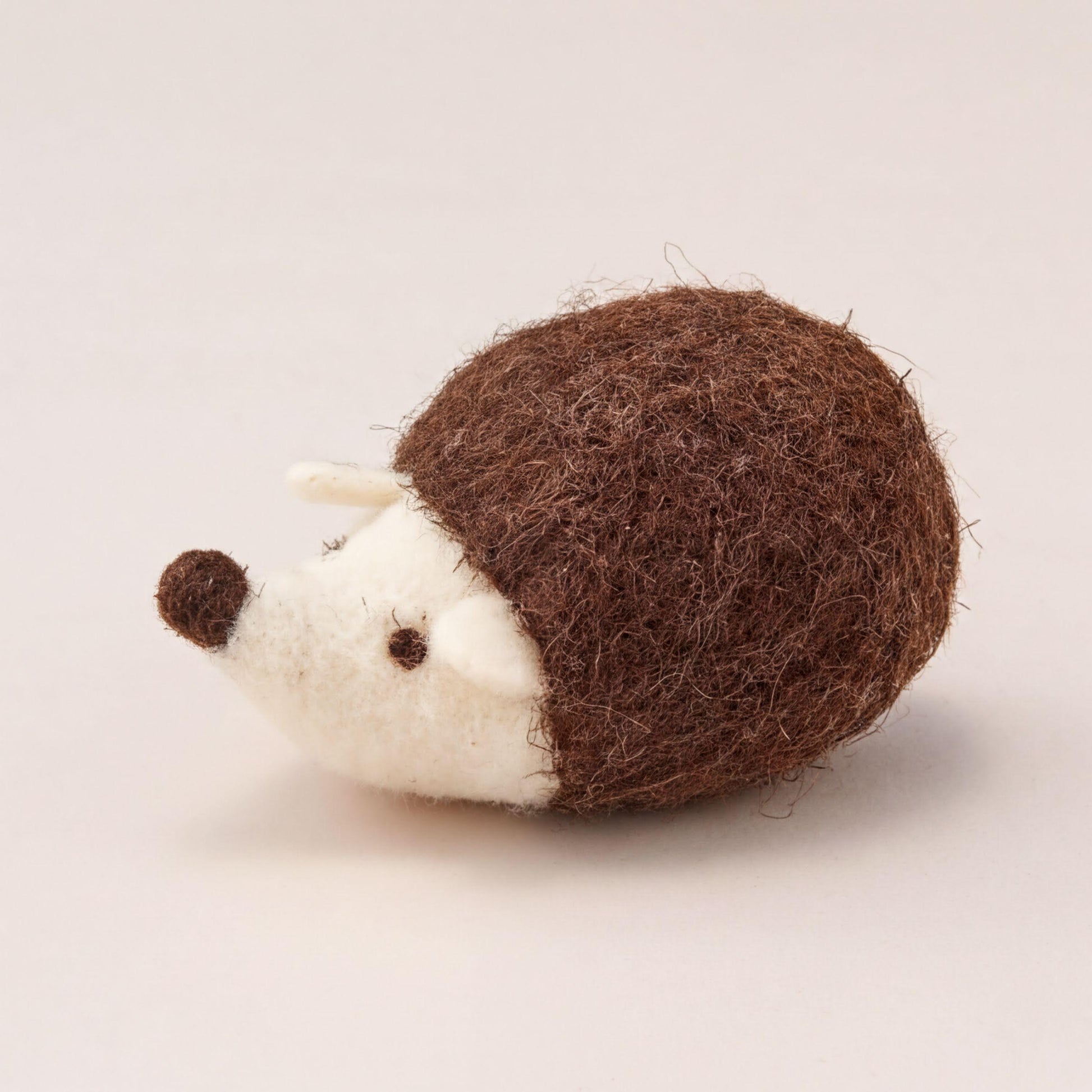 A brown and white felt hedgehog toy is sitting on a plain white surface.