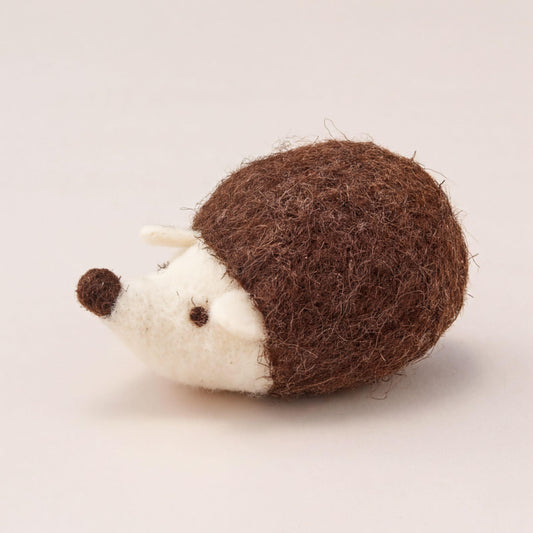 A brown and white felt hedgehog toy is sitting on a plain white surface.
