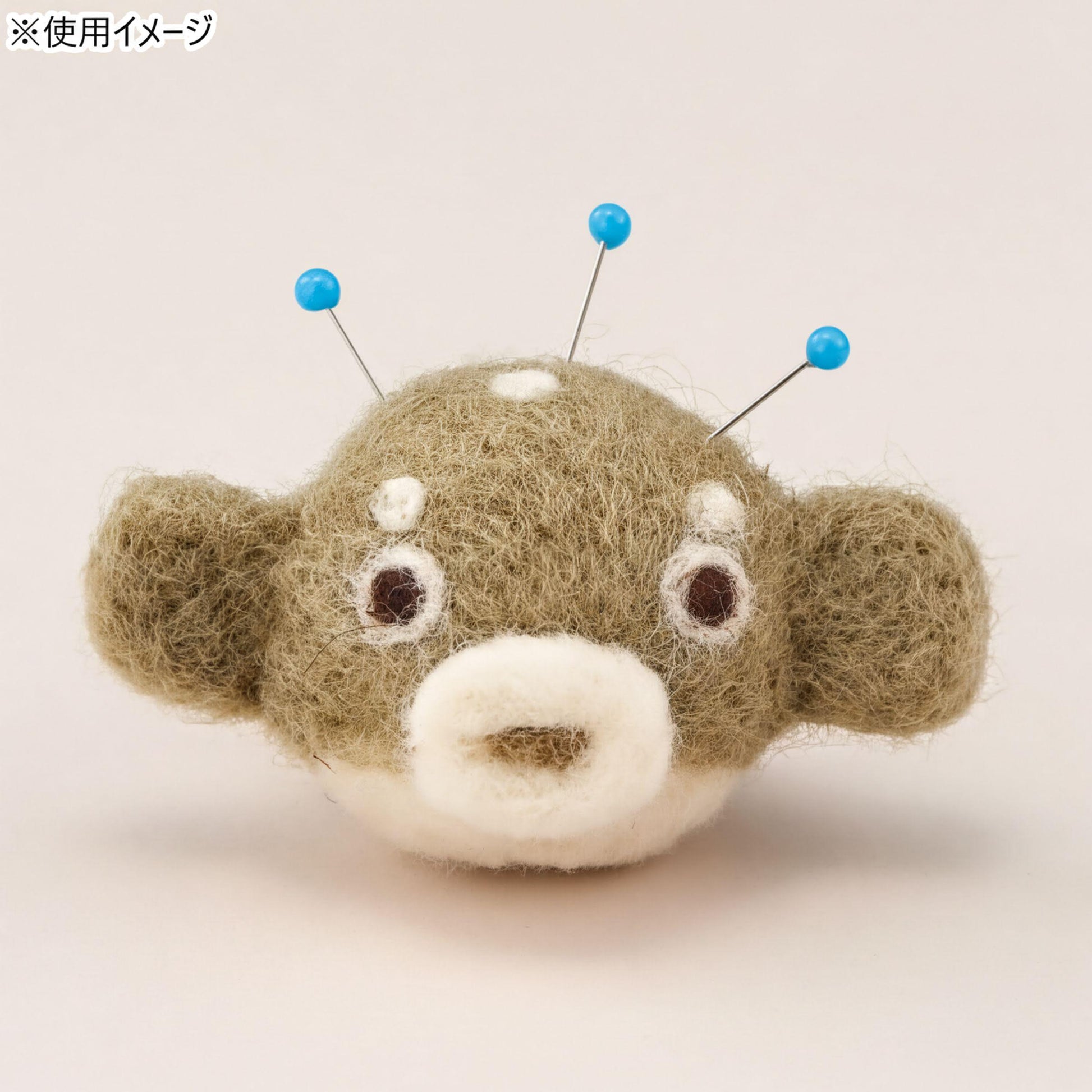 A fuzzy, brown and white stuffed animal with blue pins sticking out of its head.
