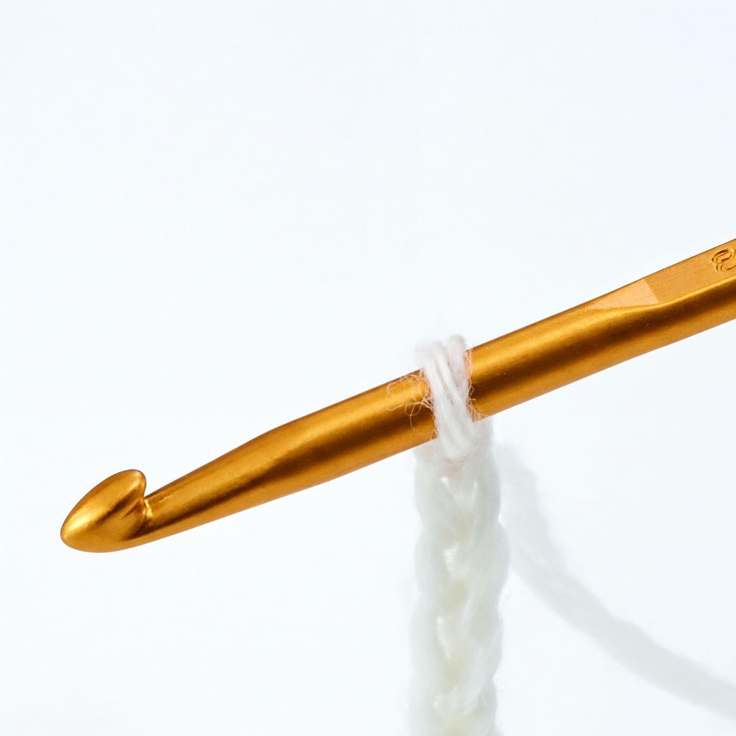 A gold crochet hook is shown in the image, with a white yarn looped around it.