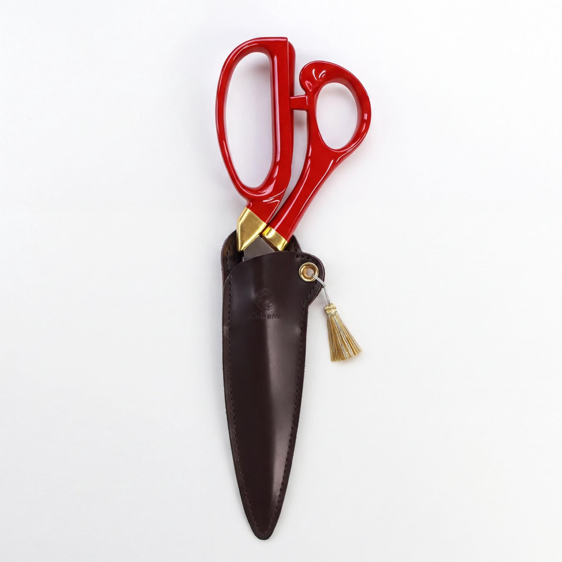 A pair of red scissors with gold accents and a tassel hanging from the handle, placed in a brown leather pouch.