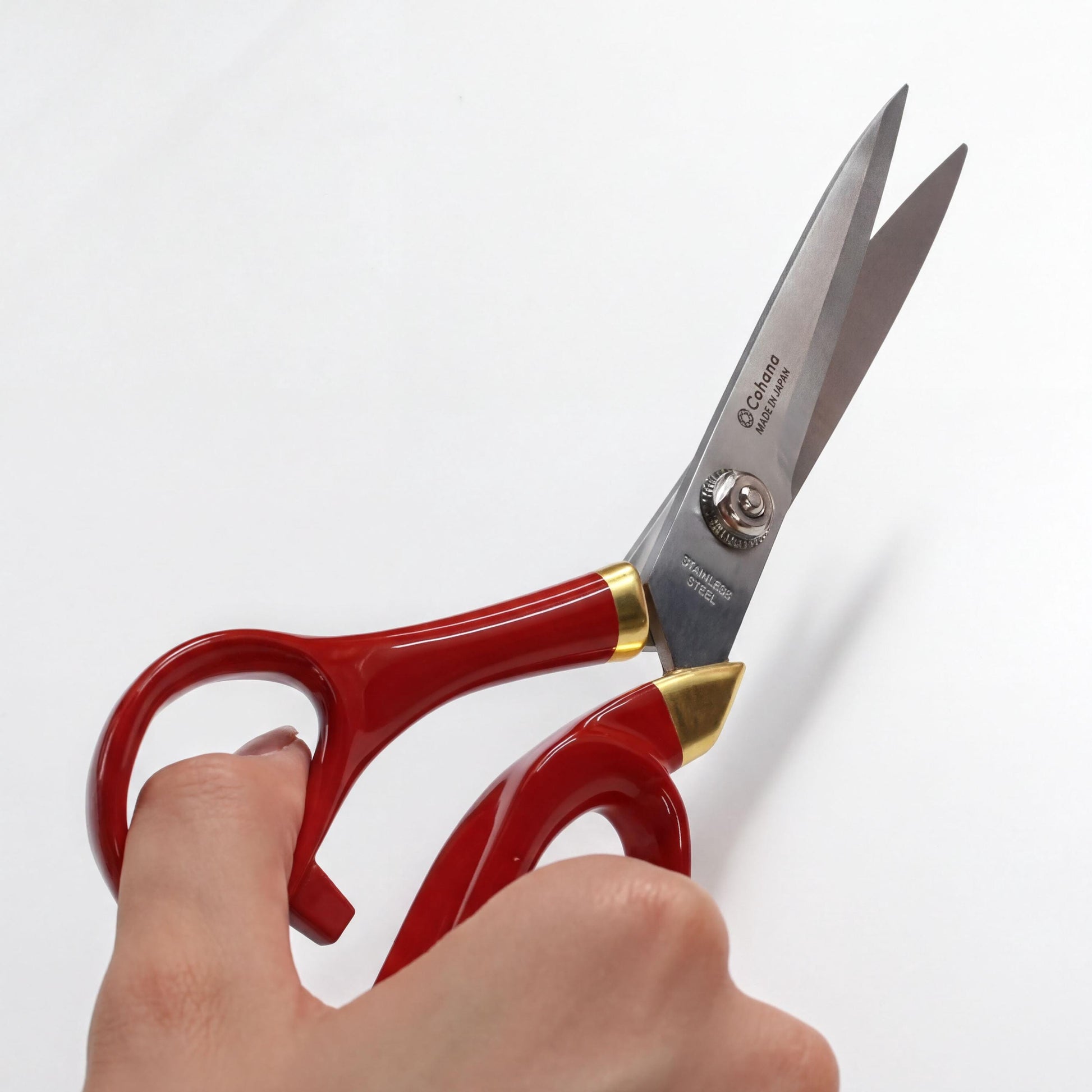 A hand holding a pair of red-handled scissors with gold accents.
