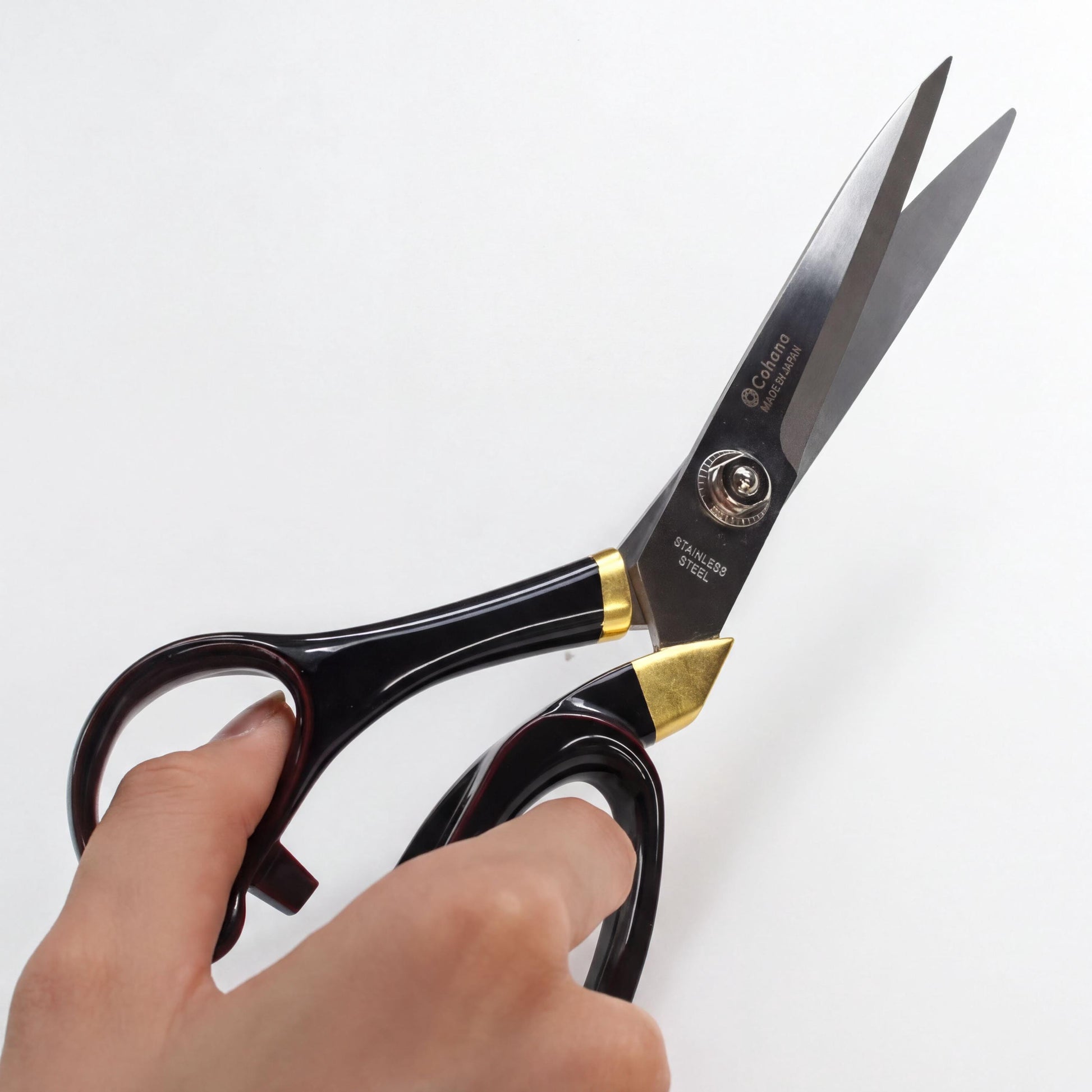 A hand holding a pair of black and gold scissors with the blades open.